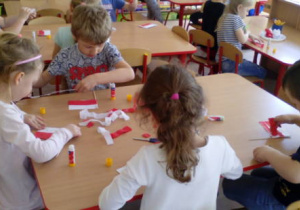 Dzieci siedzące przy stoliku podczas wykonywania flagi na patyczku.